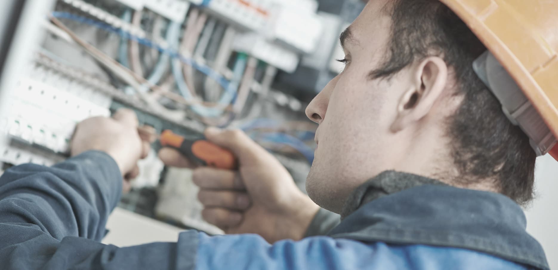 An electrician in a hard hat working on an electrical panel